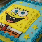 A colorful SpongeBob Cake featuring SpongeBob CakePants' cheerful face, with bright yellow frosting, vibrant blue eyes, and iconic red tie details.