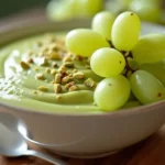 Pistachio Pudding Recipe with Grapes served in a glass bowl, topped with fresh green grapes and chopped pistachios for a creamy and nutty dessert.